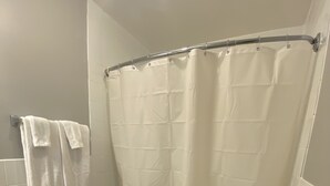 A bathroom with a toilet, a bathtub with a shower curtain, and a towel rack. - Studio 1 Motel (Cobourg)