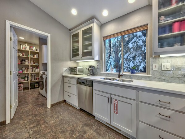 A modern kitchen with a built-in dishwasher, a window with a view of snow-covered trees, and a pantry with various food items.