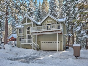 A two-story house with a garage, surrounded by snow-covered trees.