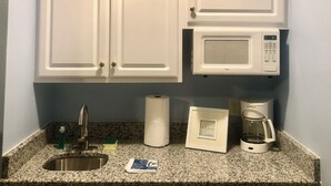 Una cucina con mobili bianchi, un lavello in acciaio inossidabile, un forno a microonde, una macchina da caffè e un rotolo di carta assorbente.