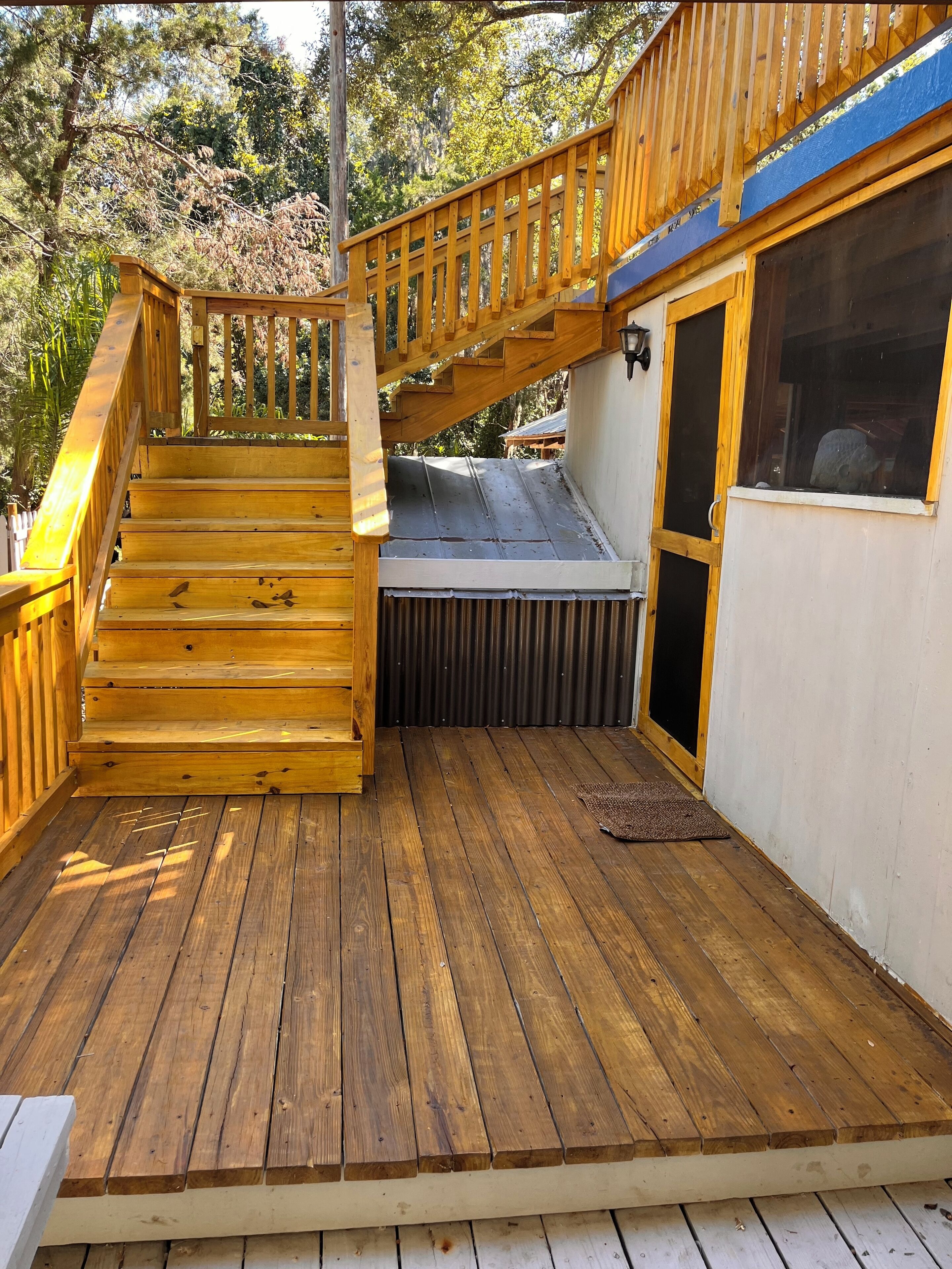 A wooden deck with a staircase leading to a covered area, surrounded by trees.