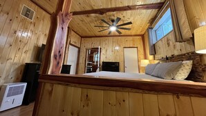 Una camera in una baita di legno con un letto, una ventola a soffitto, una finestra e una porta.