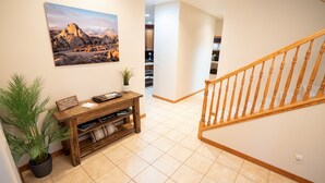 A hallway with a wooden console table, potted plants, and a painting of a mountainous landscape.
