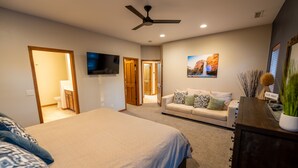A bedroom with a large bed, a sofa, a TV, and a ceiling fan.