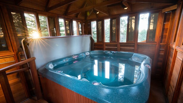 A hot tub in a wooden cabin with a wooden deck and large windows.