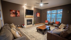 A modern living room with a fireplace, large windows, and a ceiling fan.