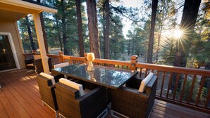 A wooden deck with wicker furniture and a glass table, surrounded by tall trees.