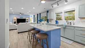 A modern kitchen with a central island, bar stools, and a ceiling fan. - Captain  ’s Quarters - Private Beach Access! (Atlantic Beach)