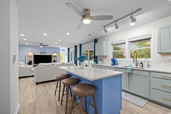 A modern kitchen with a central island, bar stools, and a ceiling fan. - Captain’s Quarters - Private Beach Access! (Atlantic Beach)
