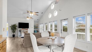 A modern kitchen with a dining area, white cabinetry, a ceiling fan, and a large window with blinds. - Captain’s Quarters - Private Beach Access! (Atlantic Beach)
