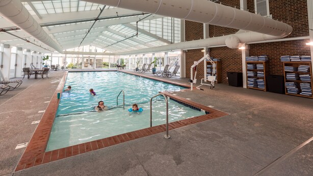 Una piscina interior con agua cristalina, un trampolín y sillones de descanso.