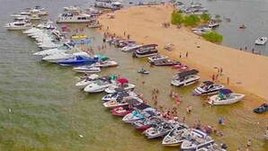 A marina with numerous boats docked along the shoreline, a sandy beach, and a calm body of water.