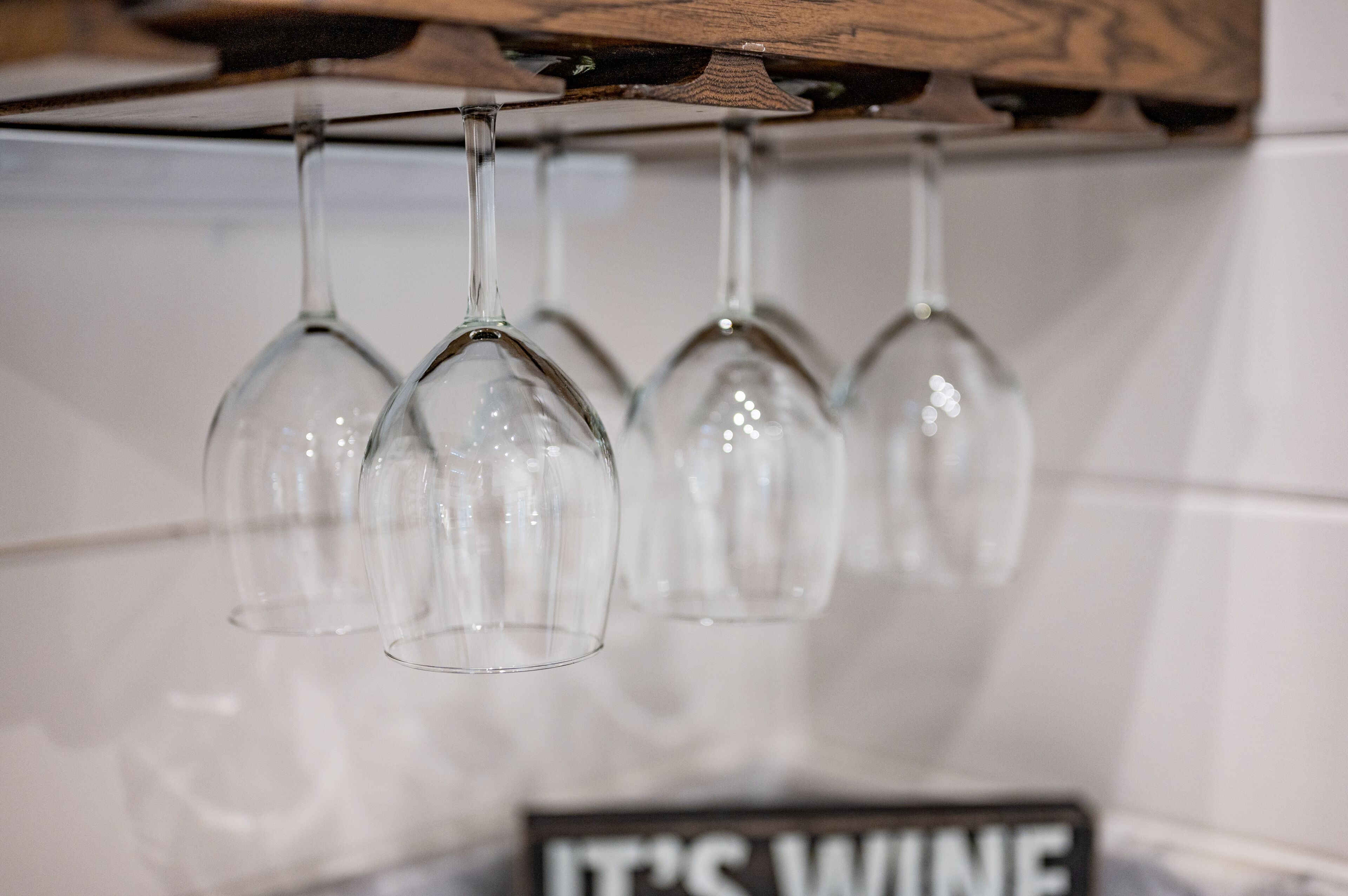 A row of empty wine glasses hanging from a wooden beam.