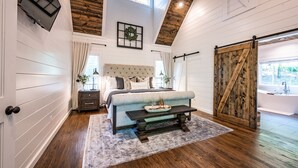 Une chambre avec un grand lit, un plafond en bois, une porte coulissante de style grange et une vue sur l’extérieur.