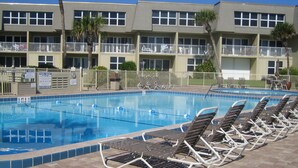 Ein Swimmingpool mit Liegestühlen, einer Pflasterterrasse und einem Gebäude mit Balkonen im Hintergrund.