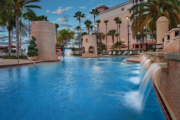 Relax by the resort pool surrounded by palm trees and lounge chairs.