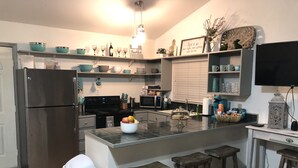 A modern kitchen with stainless steel appliances, a central island with stools, and decorative items on shelves. - PET FRIENDLY MAIN STREET LOFT, WALKING DISTANTANCE TO OLD TOWN TOMBALL (Tomball)