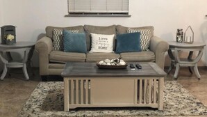 A living room with a beige sofa, two patterned pillows, a coffee table with a bowl and remote controls, and a rug. - PET FRIENDLY MAIN STREET LOFT, WALKING DISTANTANCE TO OLD TOWN TOMBALL (Tomball)