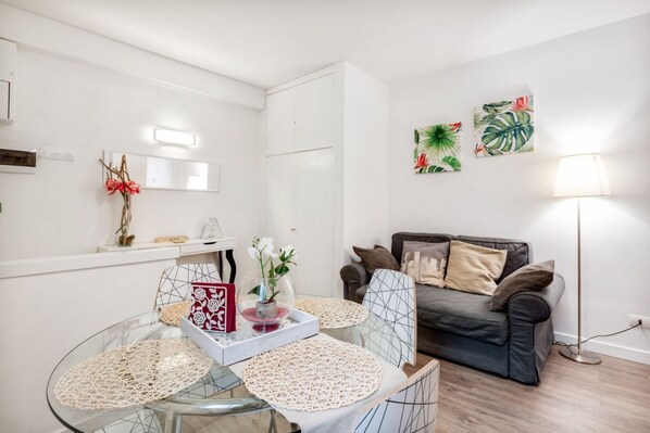 A modern living room with a glass dining table, a sofa, and wall art.