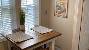 A dining area with a wooden table and chairs, a potted plant, and a wall-mounted poster.