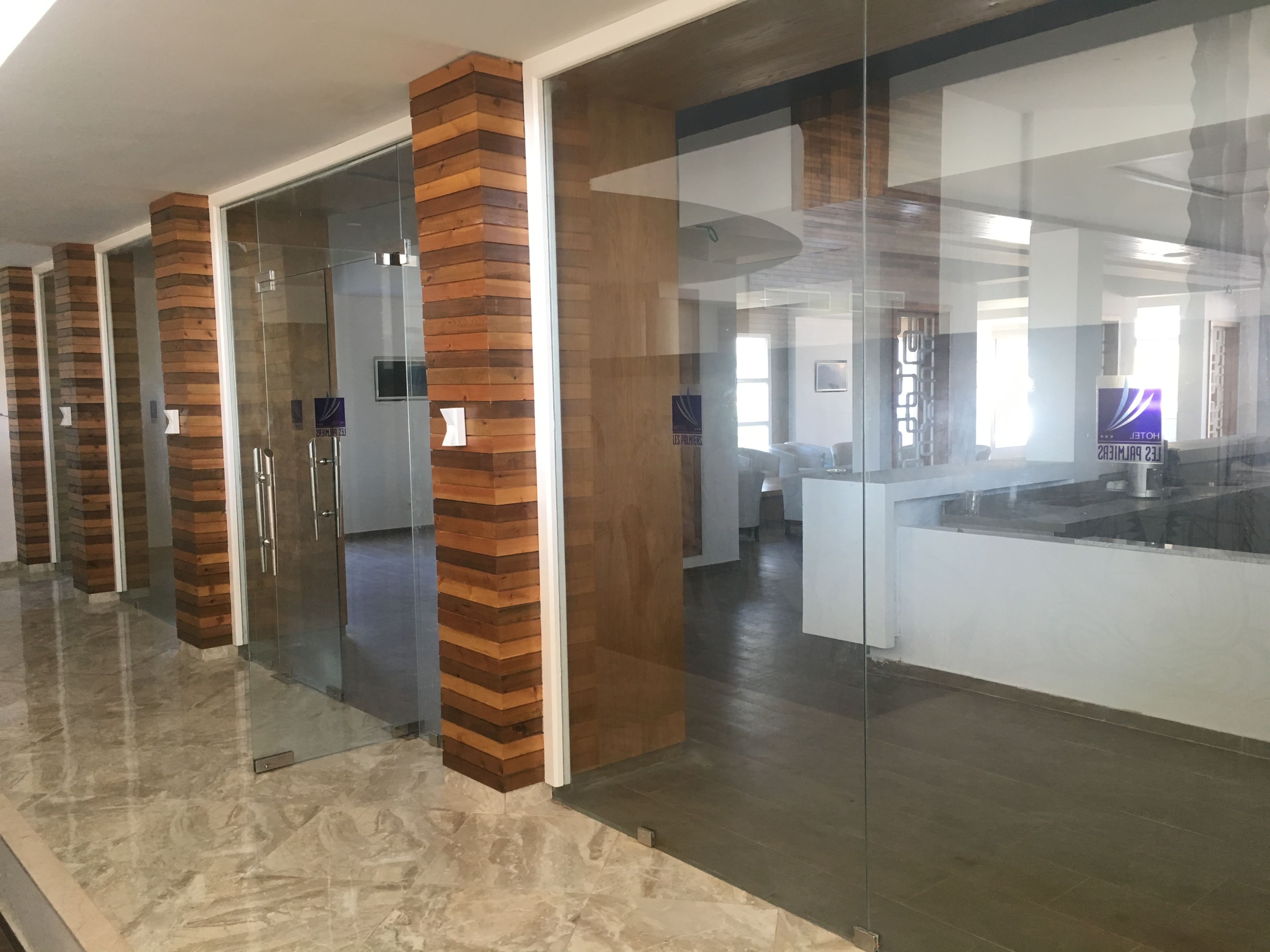 Un hall d’hôtel moderne avec des cloisons en verre, des éléments décoratifs en bois et un comptoir d’accueil.