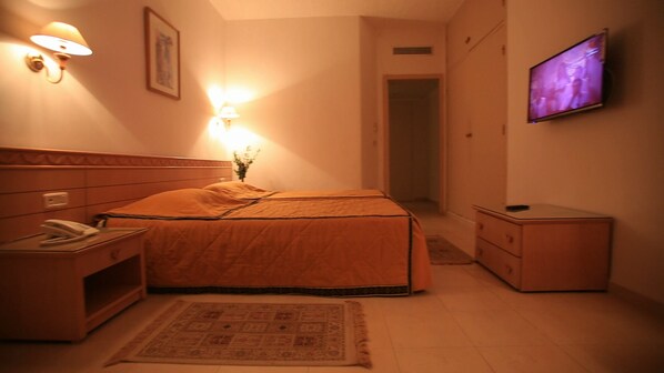 Una habitación de hotel con cama, mesita de noche, lámpara, televisor y un armario pequeño.