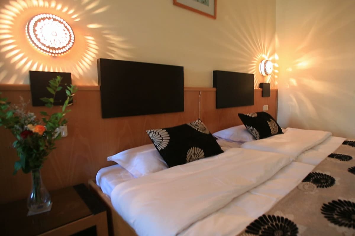 A hotel room with a bed, two wall-mounted speakers, and a decorative light fixture.