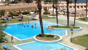 A large outdoor swimming pool with multiple lanes, surrounded by palm trees and lounge chairs. - Les Palmiers (Monastir)