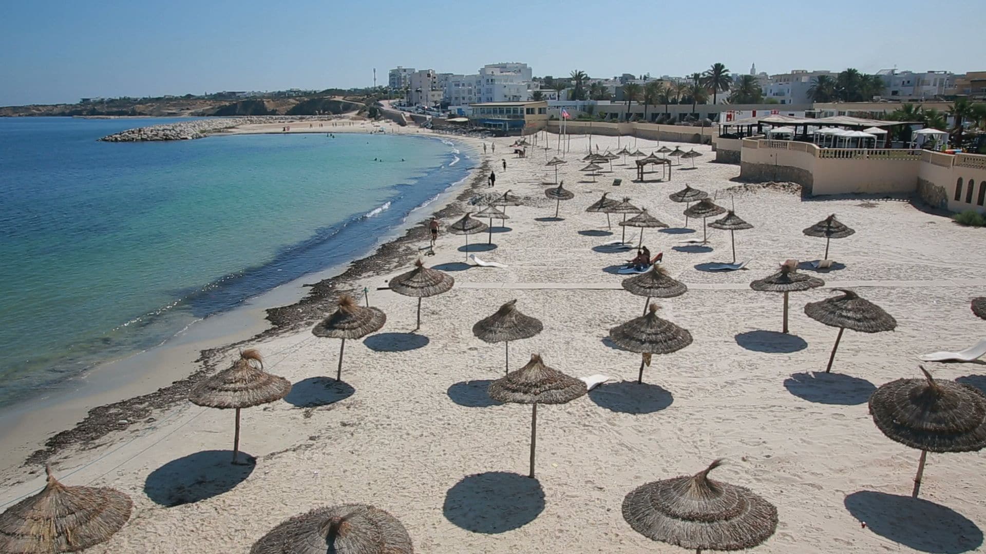 Una playa con hileras de sombrillas de paja y una vista despejada del mar.