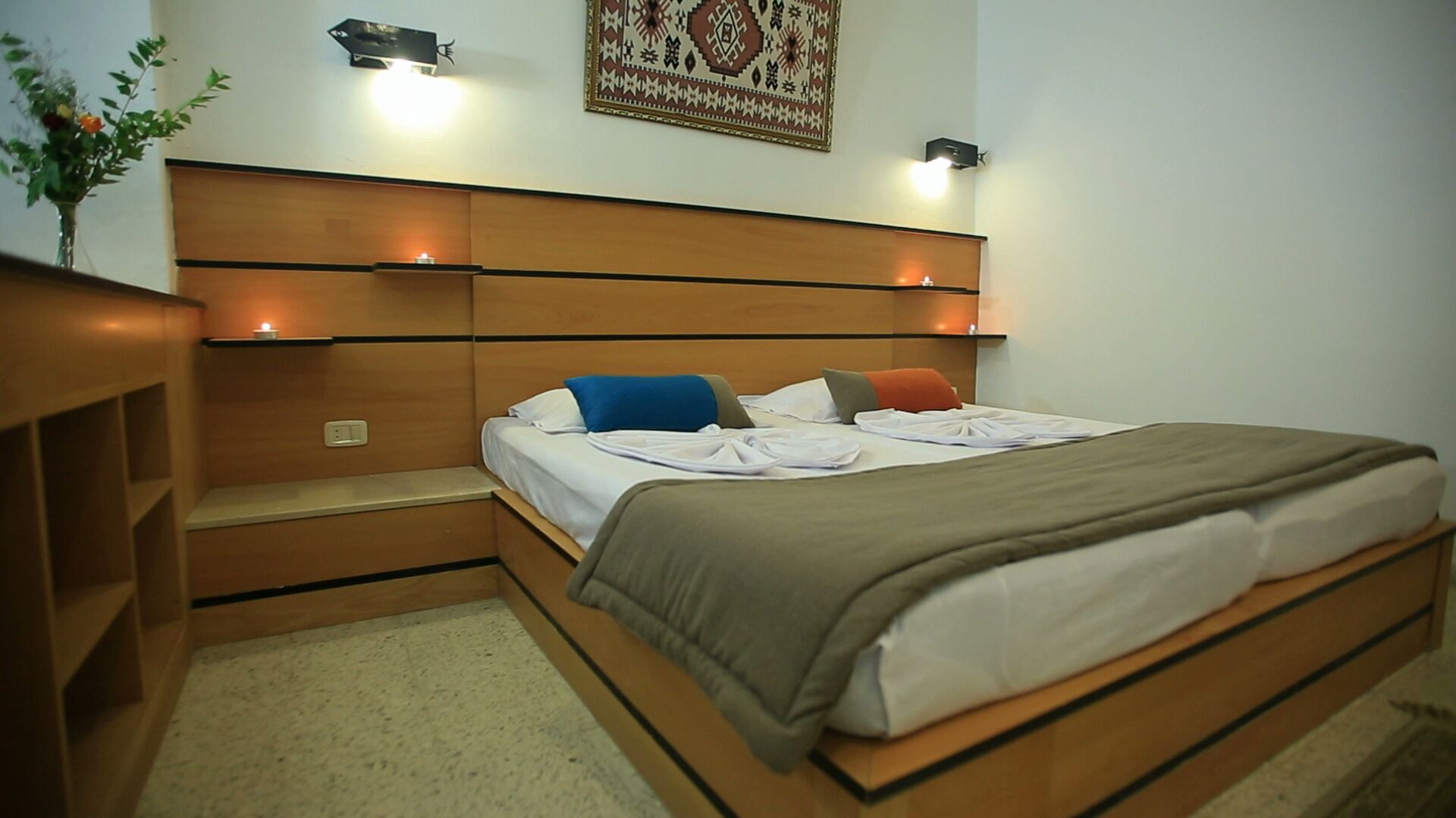 Una habitación de hotel con cabecera de madera, cama con ropa blanca y una mesita de noche pequeña.
