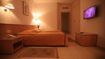 A hotel room with a bed, bedside table, lamp, TV, and a small cabinet.