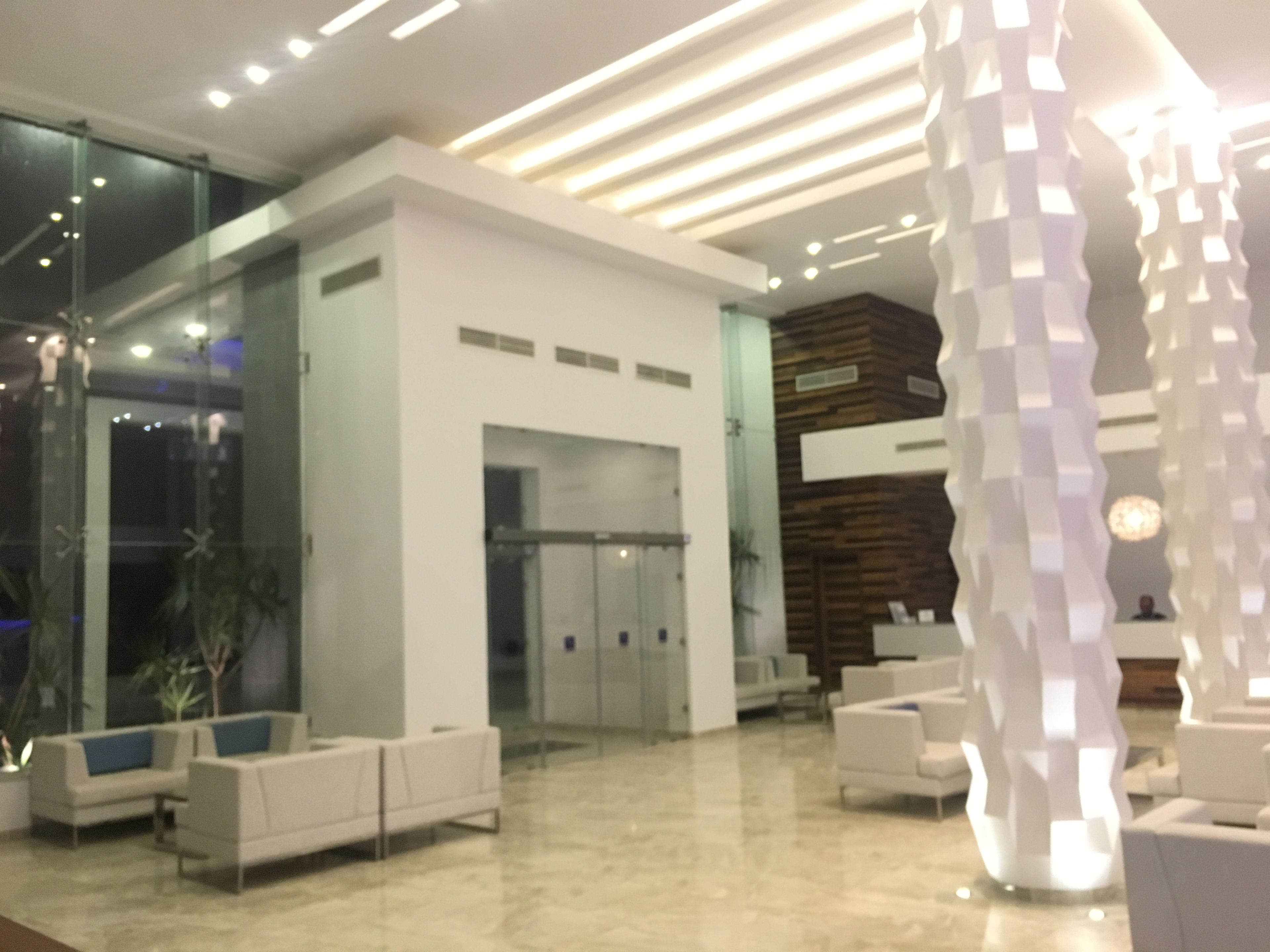 A modern lobby with a reception desk, seating area, and glass doors leading to other rooms.