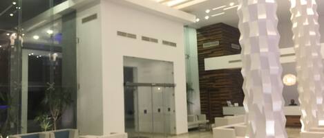 A modern lobby with a reception desk, seating area, and glass doors leading to other rooms.