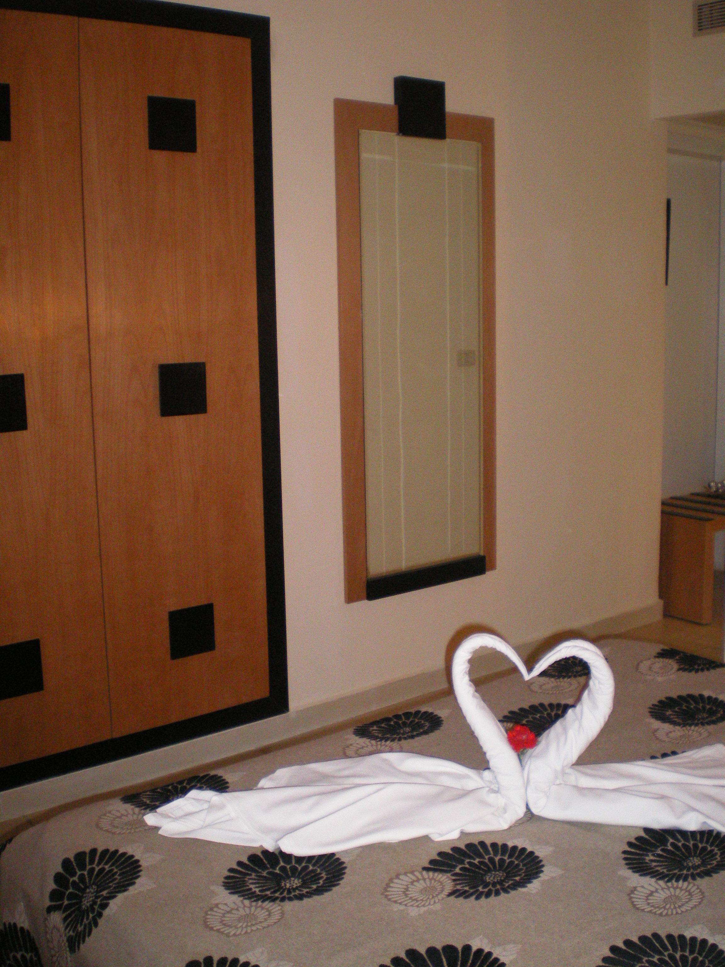 A hotel room with a bed, a mirror, and a wooden wardrobe.
