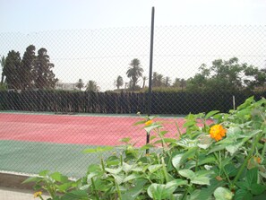 Una cancha de tenis con una cerca de malla metálica, rodeada de follaje y árboles.