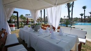 An outdoor dining area with white tablecloths, a large silver bowl, and bottles of water.