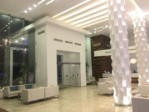 Un vestíbulo moderno con mostrador de recepción, zona de estar y puertas de vidrio que dan a otras salas.