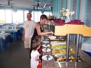 A buffet setup with multiple food stations and a person serving food. - Les Palmiers (Monastir)