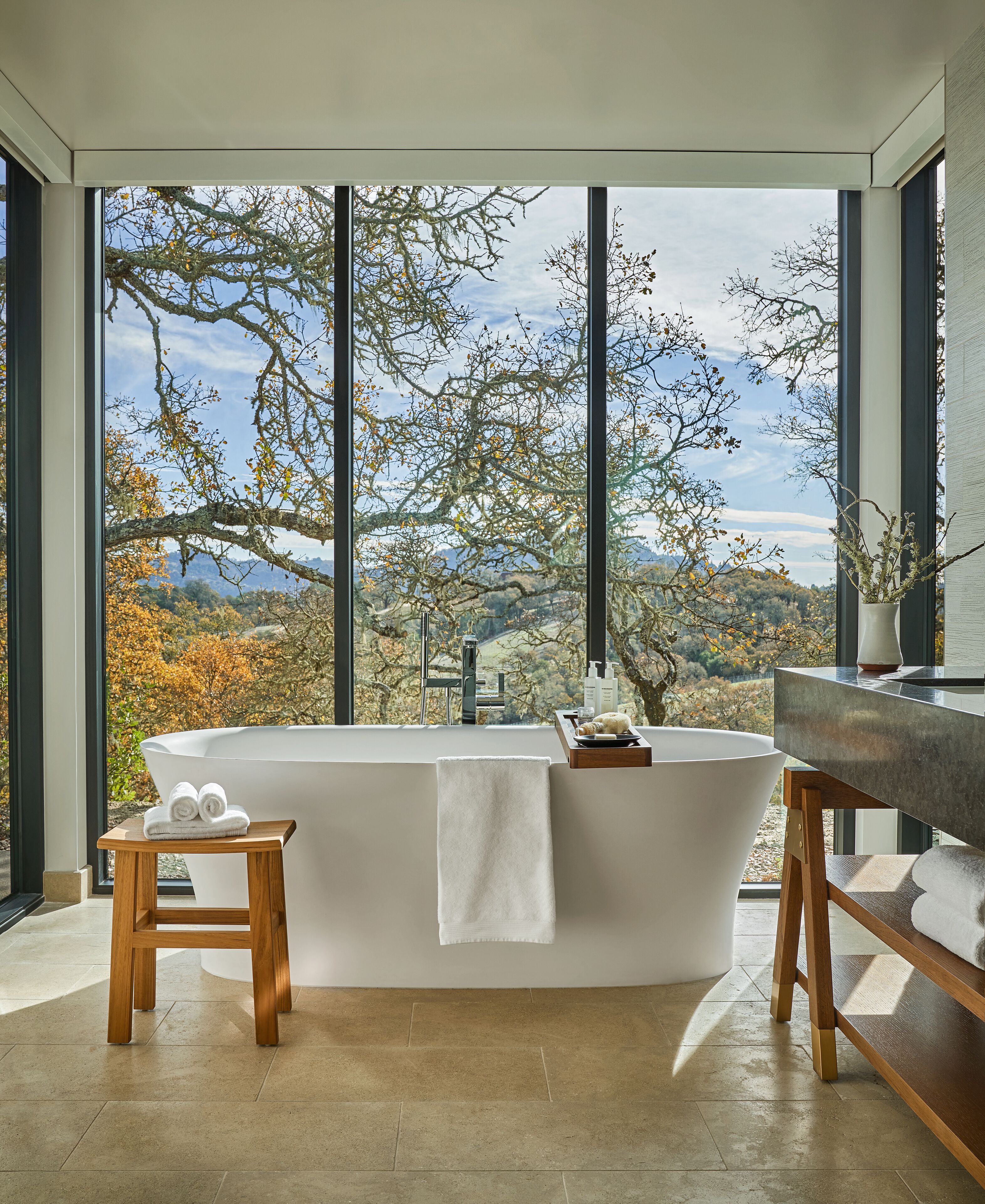 A modern bathroom with a freestanding bathtub, a wooden stool, and a vanity with a mirror.