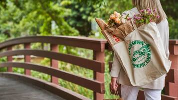 A person holding a bouquet of flowers and a shopping bag with a logo on a wooden bridge.