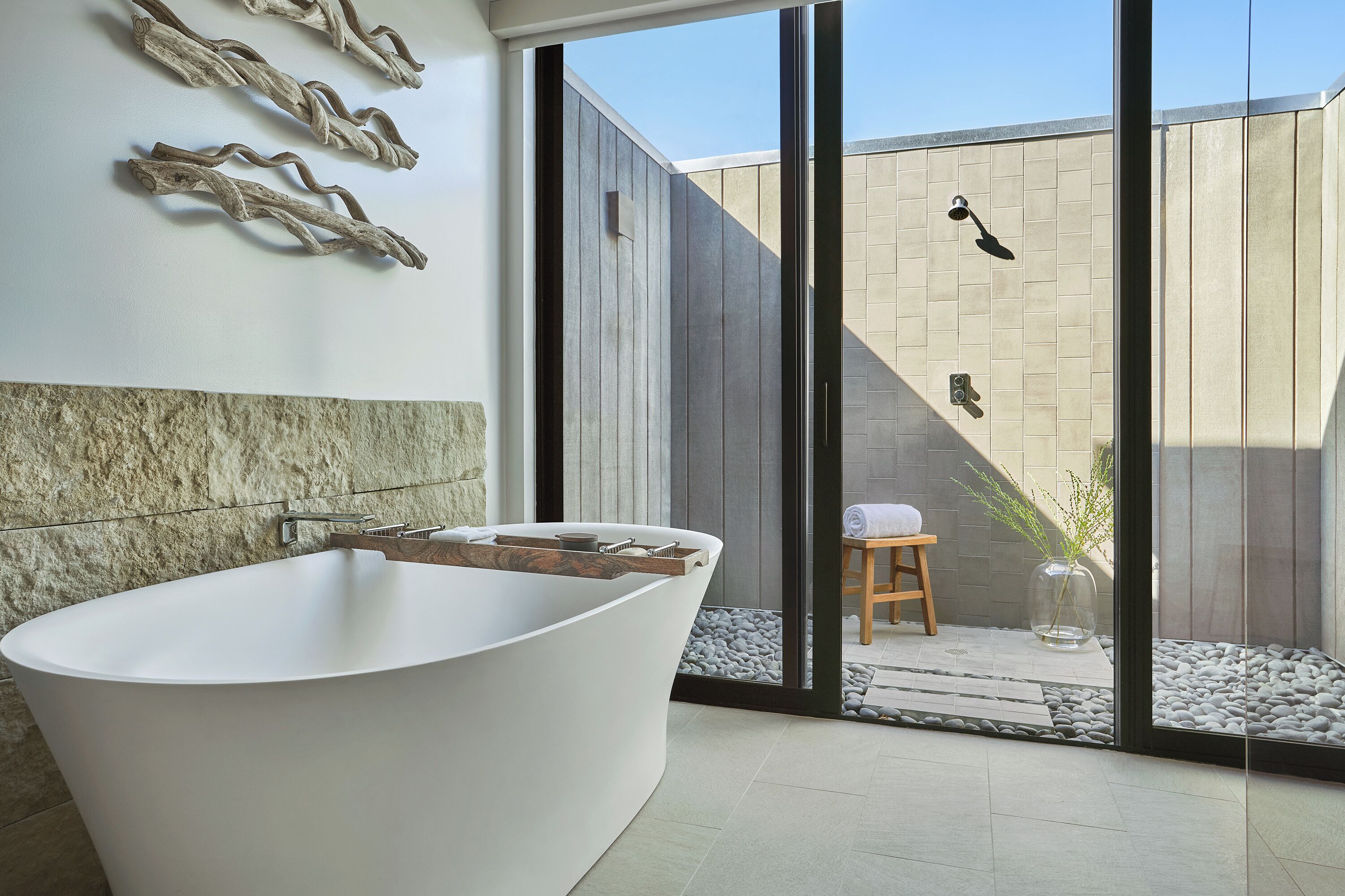 Ein modernes Badezimmer mit einer freistehenden Badewanne, einem Holzschemel und einem kleinen Tisch mit einer Pflanzvase.