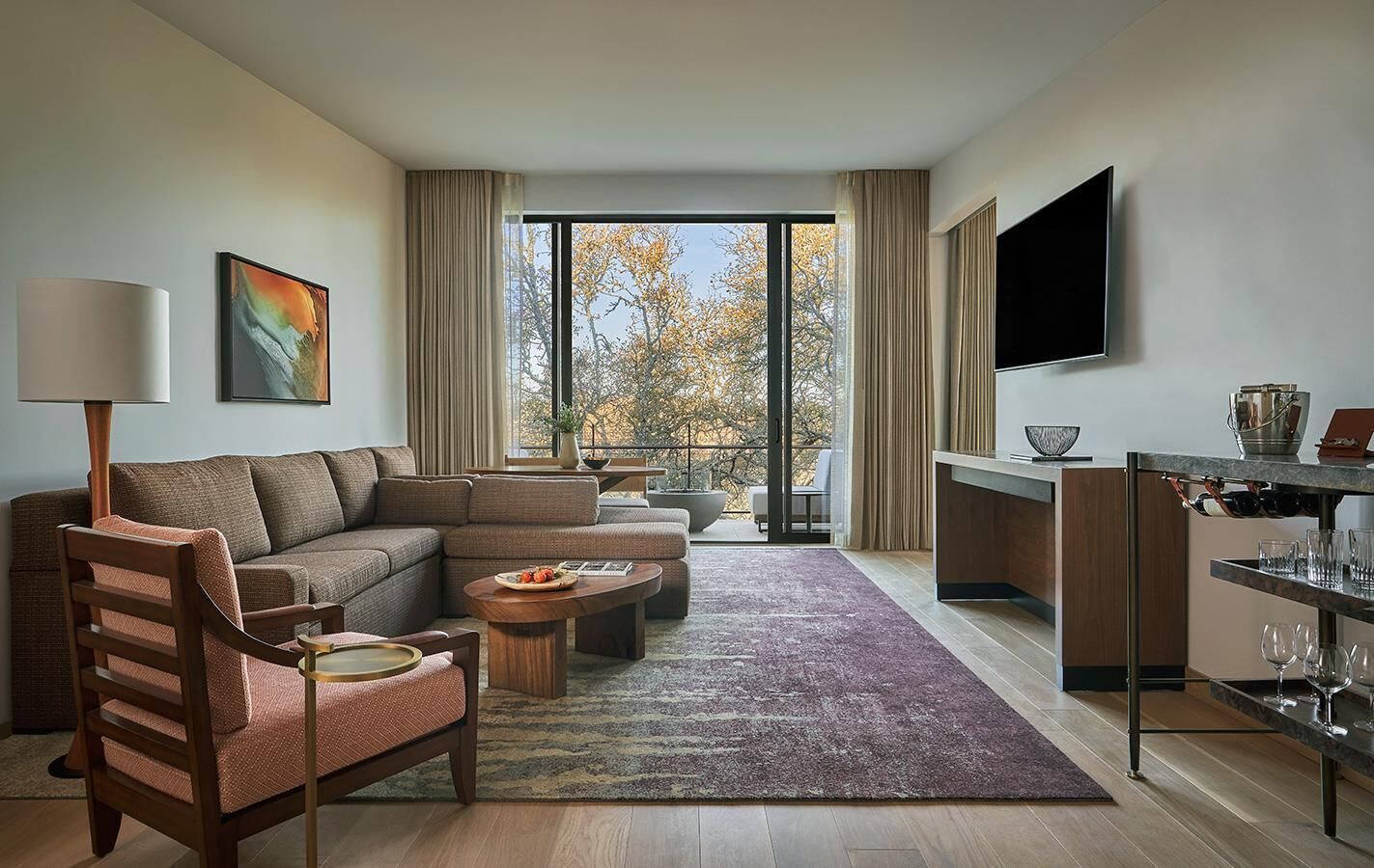 Una sala moderna con un sofá seccional, una silla de madera, una mesa de centro y un televisor montado en la pared.