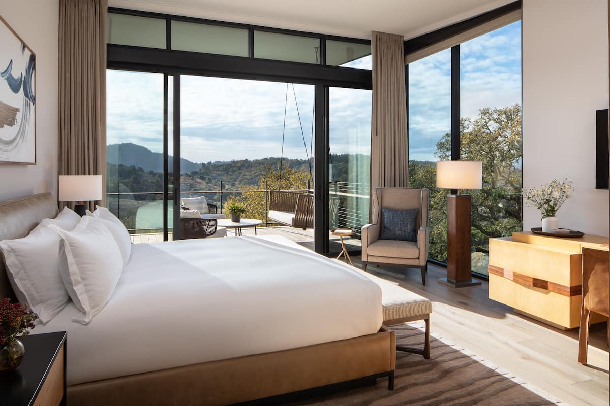 A modern hotel room with a large bed, a seating area with a view, and a wooden desk.