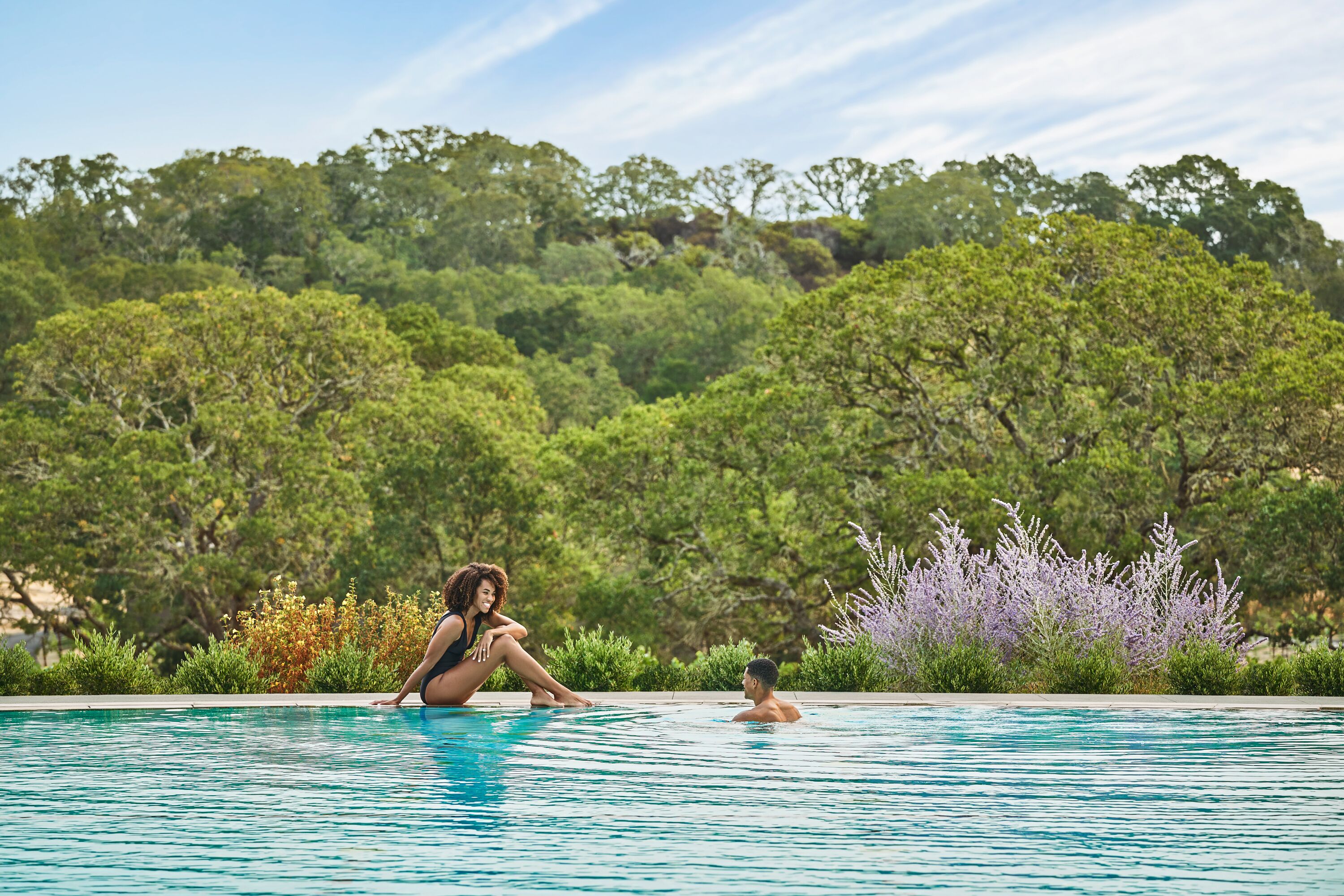 Piscina con dos personas, rodeada de exuberante vegetación y árboles.