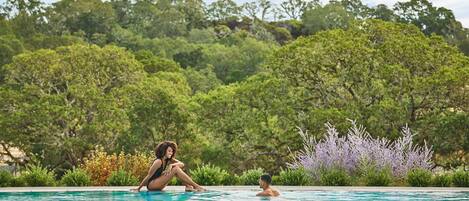Piscina con dos personas, rodeada de exuberante vegetación y árboles.