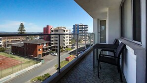 A balcony with a view of a tennis court, buildings, and a clear sky.
