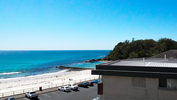 A beach view with a parking lot and a building with a flat roof.