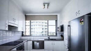 A modern kitchen with white cabinets, stainless steel appliances, and a large window offering a view of a high-rise building.