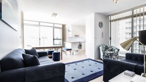 A modern living room with dark blue sofas, a coffee table, and a large window with a city view.