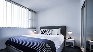 A modern bedroom with a large bed, two bedside tables with lamps, and a window with blinds.